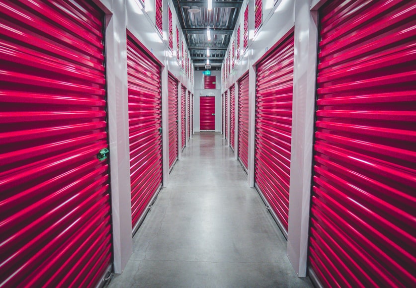 A hallway of an indoor climate-controlled storage facility with red doors on units for rent.