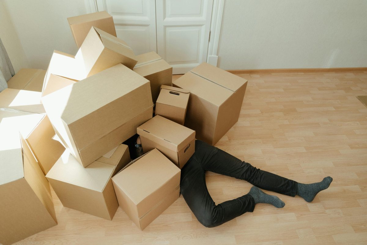 Person laying under brown cardboard boxes on brown wooden floor