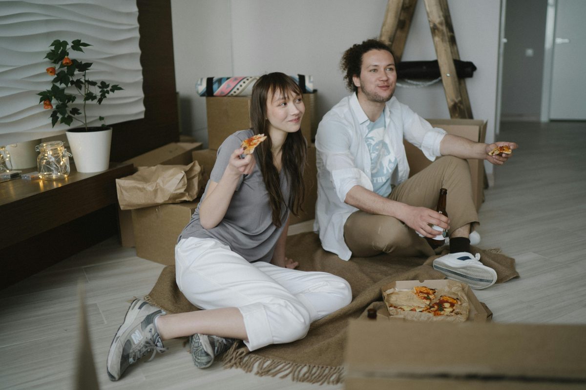 A couple sitting on the floor eating pizza after moving in