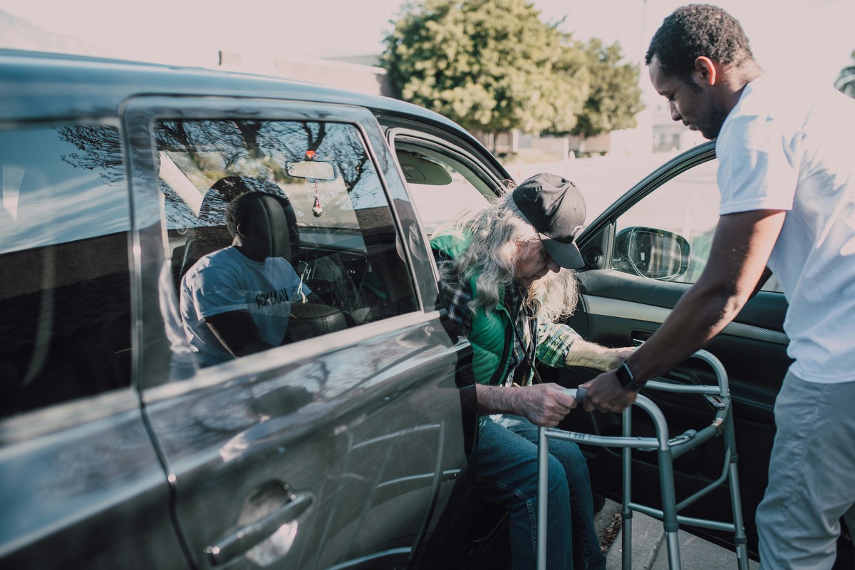 A young man helping a senior with a walker out of a car