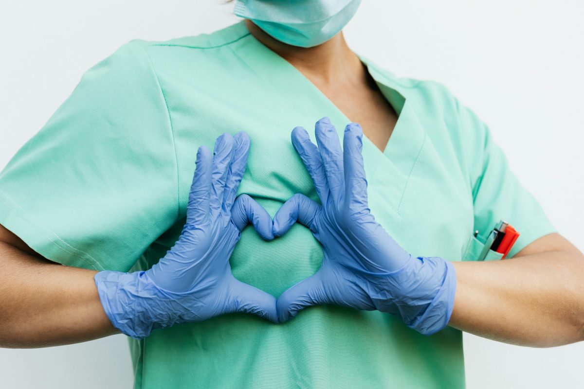 A person wearing medical gloves doing heart shape