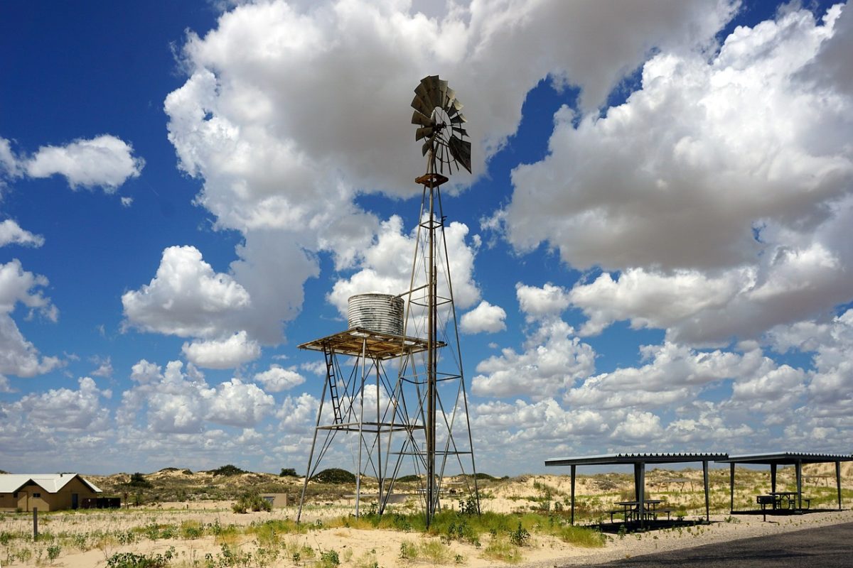 A flat field in Texas with a windmill and some shrubs