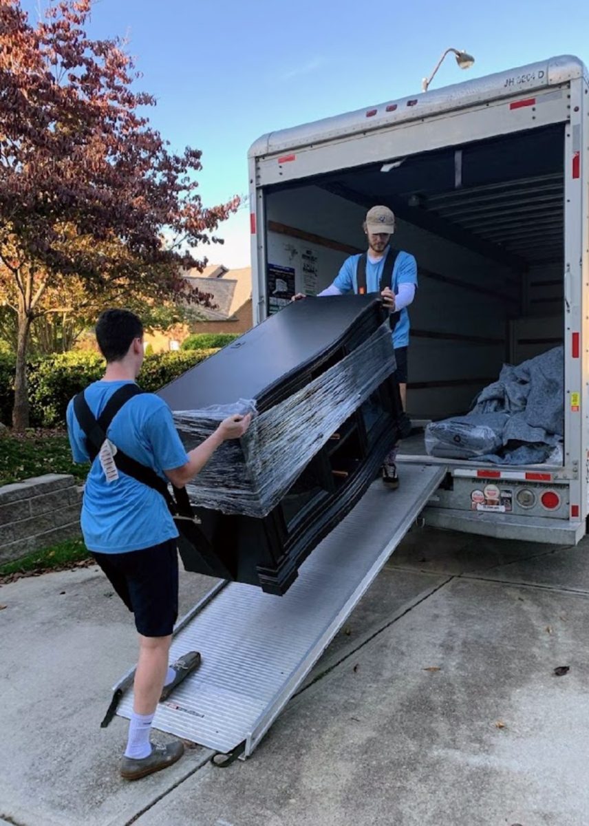 Two people moving a large, heavy piece of furniture with lifting straps
